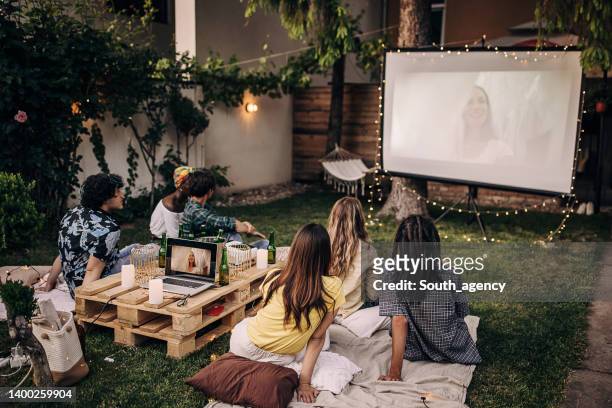 group of friends having a gathering, watching a movie on projector in the garden and hanging out - outside cinema stockfoto's en -beelden