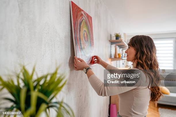 young female artist hanging her art on the wall - wall art stock pictures, royalty-free photos & images