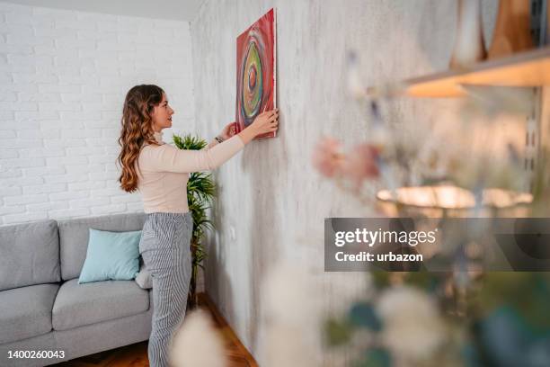 young female artist hanging her art on the wall - hanging art stock pictures, royalty-free photos & images