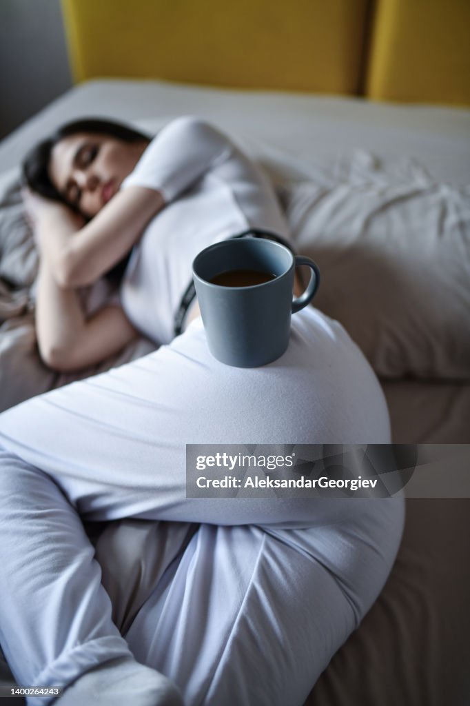Female Placing Coffee Cup On Buttock After Relaxing In Bed At Home