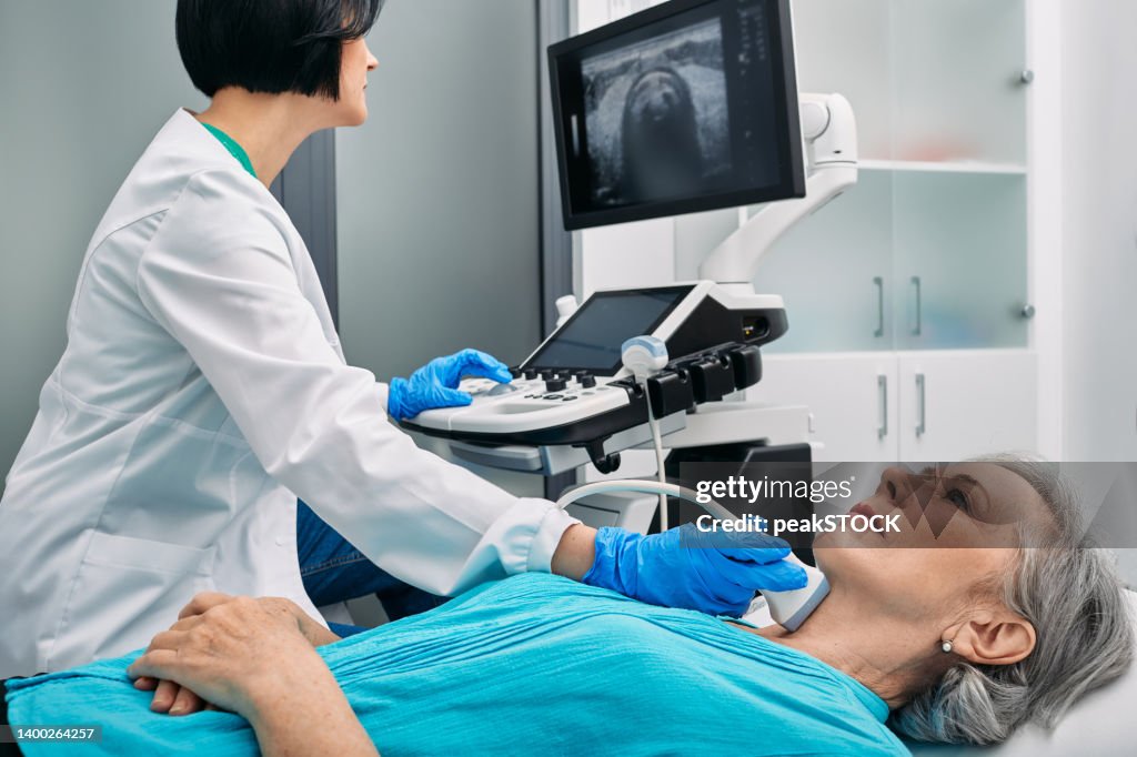 Ultrasound diagnostics of thyroid gland. Endocrinologist making ultrasonography to senior female patient at ultrasound office of medical clinic