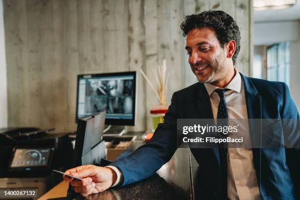 un hombre de negocios está pagando con tarjeta de crédito en la recepción del hotel - vestíbulo edificio de transporte fotografías e imágenes de stock