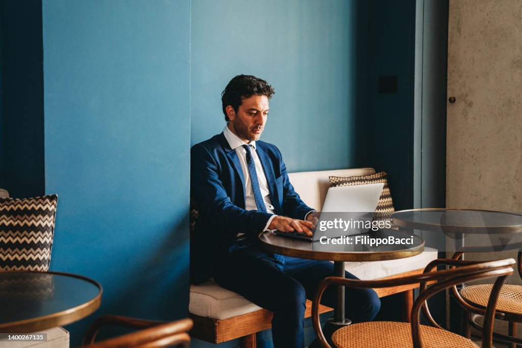 Ein Geschäftsmann arbeitet mit seinem Laptop, während er auf einem Tisch im Café sitzt