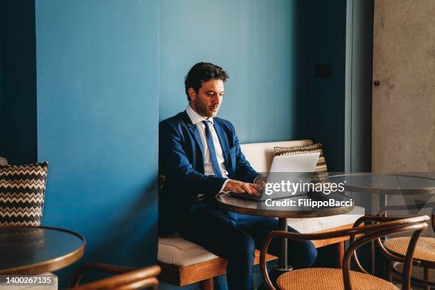 a businessman is working with his laptop while he's sitting on a table in café - conference lobby stock pictures, royalty-free photos & images