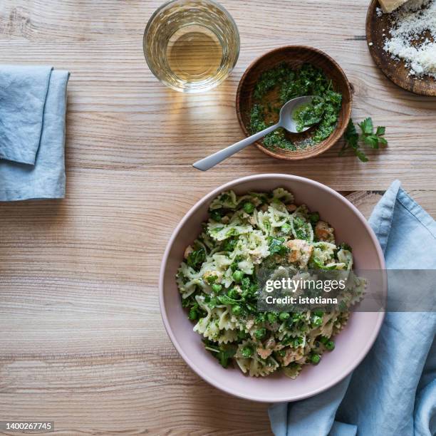 bowl of bow tie pasta with parsley pesto and  parmesan cheese on wooden table - bow tie pasta stock pictures, royalty-free photos & images