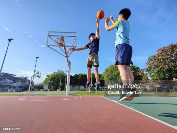 backlit asian chinese father jumping blocking son shooting playing basketball outdoors during weekend morning - chinese teenage boy stockfoto's en -beelden