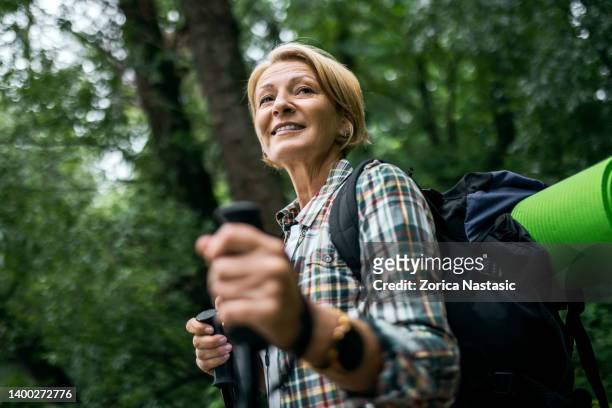 mid adult woman in the forest hiking with hiking poles - hiking pole stockfoto's en -beelden