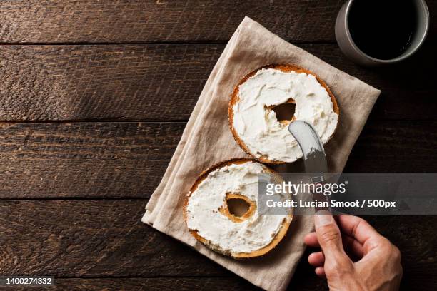 cropped hand of person with bagel with cream cheese breakfast - bagel stock-fotos und bilder