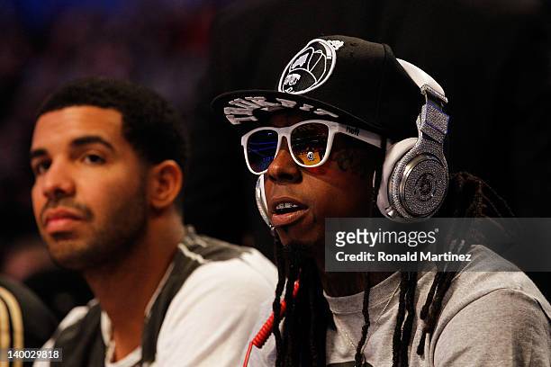 Hip-hop artists Lil' Wayne, wearing diamond studded beats headphones by Dr. Dre and Drake sit courtside during the 2012 NBA All-Star Game at the...