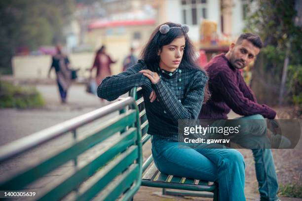 sad young woman and a man sits together o a park bench. - relationship difficulties stock pictures, royalty-free photos & images