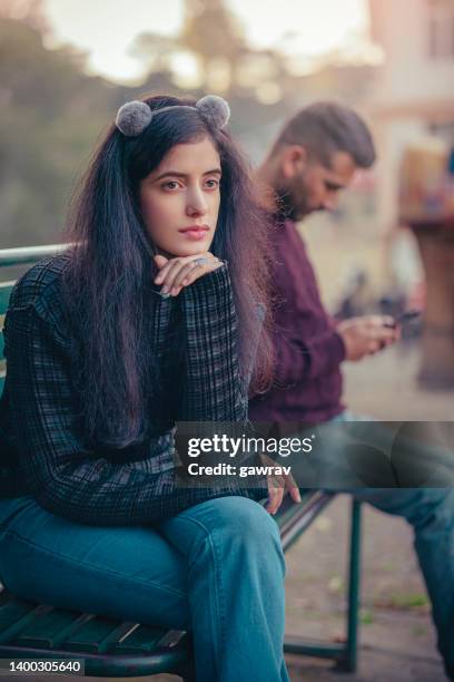 sad young woman and a man sits together o a park bench. - relationship breakup stock pictures, royalty-free photos & images