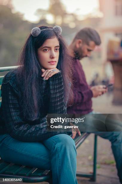 sad young woman and a man sits together o a park bench. - couple breakup stock pictures, royalty-free photos & images