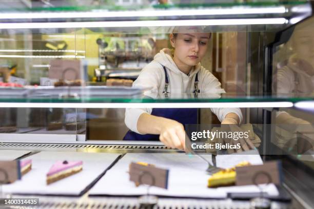 young woman coffee shop employee placing cake in bakery refrigerator - deeltijdbaan stockfoto's en -beelden