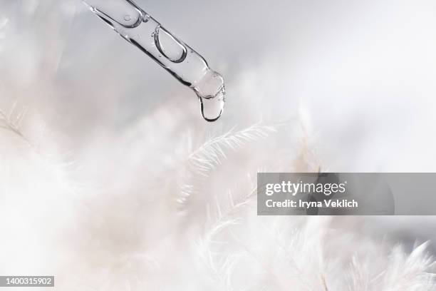 close-up pipette with face serum or essential oil with oxygen aqua bubbles and a drop of liquid against the background of delicate and soft feathers. - falling feathers stock pictures, royalty-free photos & images