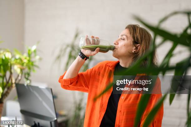 businesswoman having smoothie in her environmentalist green office - reusable water bottle office stock pictures, royalty-free photos & images