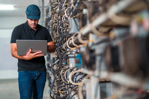 Professional engineers carrying the laptop working in crypto mine.