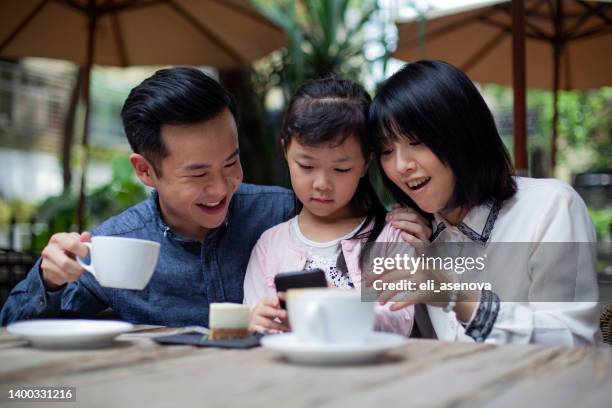 happy asian family having lunch at a restaurant and having fun with a smart phone, taipei - asian family cafe stockfoto's en -beelden