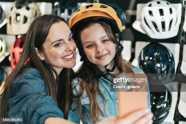 niña probándose el casco de ciclismo en la tienda de bicicletas con la madre - ropa protectora deportiva fotografías e imágenes de stock