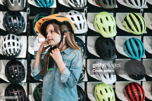 little girl trying on cycling helmet in bike shop - sports equipment store stock pictures, royalty-free photos & images