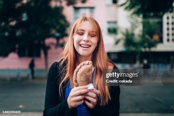 young woman eating empanada on the streets - santiago chile street stock pictures, royalty-free photos & images