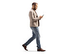 Full length profile shot of a man walking and looking at a smartphone