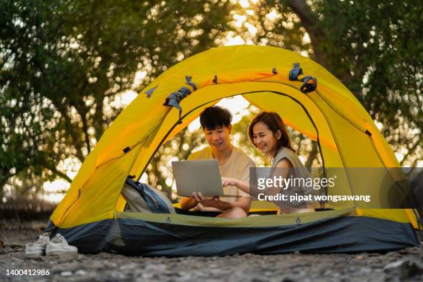 couple sitting in a tent during camping is sitting on a laptop, concept. internet is everything - east asia foto e immagini stock