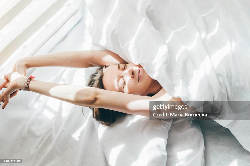 Woman sleeping under duvet at the sunny morning, top view.