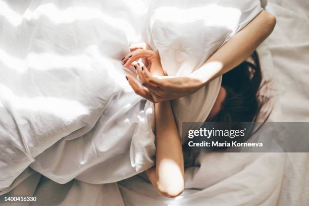 sleepless woman lying in bed hiding under duvet. - piumone foto e immagini stock
