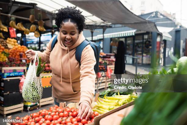 african american young woman buying veggies on the market - herbruikbare tas stockfoto's en -beelden