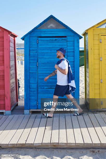 a man walking towards the beach with colored huts in the background - toalla stock pictures, royalty-free photos & images