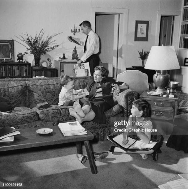 American actress Kim Hunter relaxes on the sofa with a glass of wine in her hand, her son Sean beside her, and daughter Kathryn sitting on the floor,...