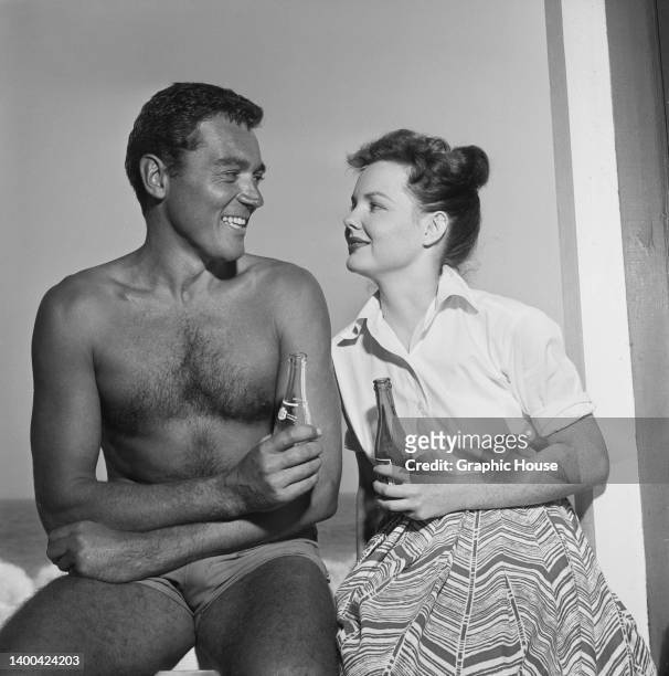 American actor William Bishop wearing only a pair of shorts, and American actress Wanda Hendrix in a white short-sleeve shirt and a patterned skirt,...
