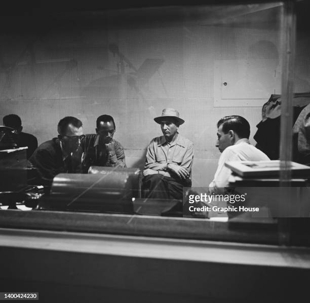 American bass player Tommy Potter and American clarinetist and bandleader Artie Shaw sitting between two men, at an recording studio in New York...