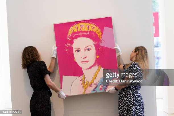 Gallery staff pose with a portrait of Queen Elizabeth II by artist Andy Warhol at Phillips auction house on June 01, 2022 in London, England....