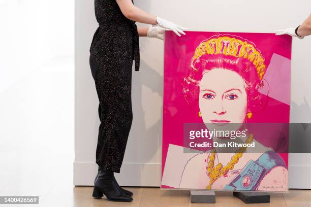 Gallery staff pose with a portrait of Queen Elizabeth II by artist Andy Warhol at Phillips auction house on June 01, 2022 in London, England....