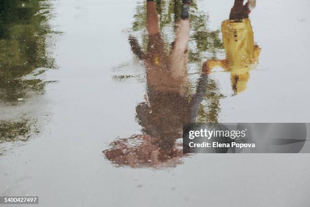 father and son walking at the city on rainy day, reflection in a puddle - laarzen geel stockfoto's en -beelden
