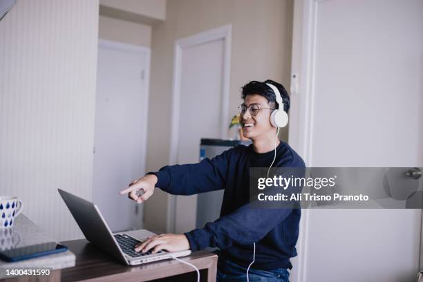 young asian man, watching live streaming, using laptop and headphone - handsome muslim men stock pictures, royalty-free photos & images