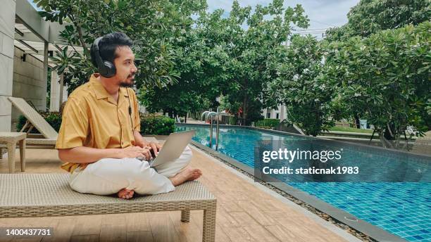 asian man using a laptop sitting near pool in summer - business social gathering poolside stock pictures, royalty-free photos & images