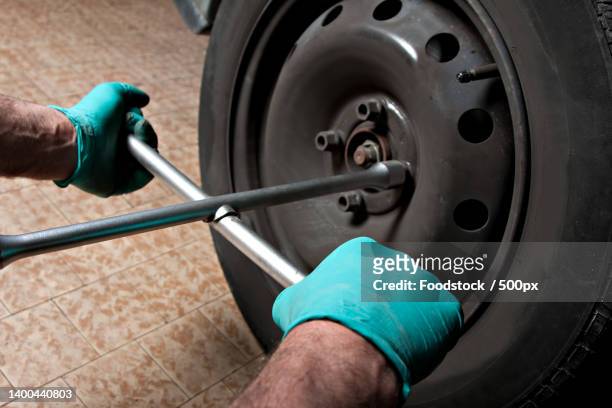 car mechanic hand using cross wrench to uninstallation the wheel nuts - car jack stock-fotos und bilder