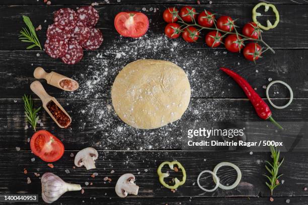 raw dough for pizza with ingredients and spices on black background - pizza ingredients stock pictures, royalty-free photos & images