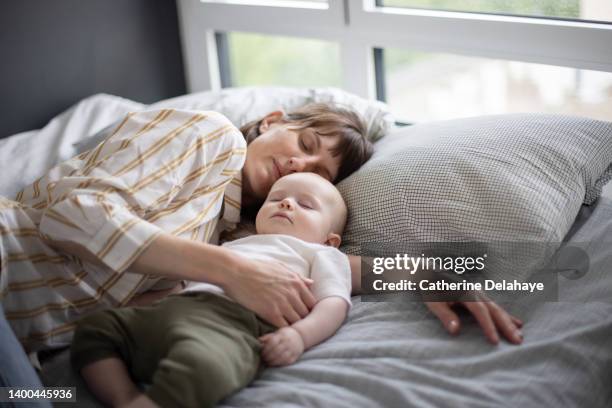 a 6 month old baby and his mum sleeping on a bed at home - mother sleeping child stock-fotos und bilder