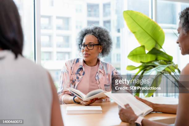 senior woman listens to her group member - book club meeting stock pictures, royalty-free photos & images