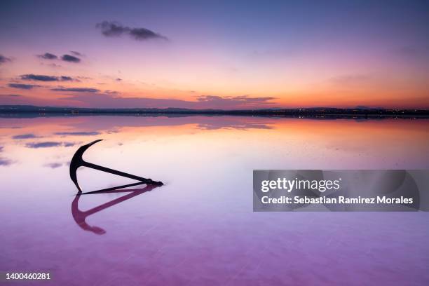 landscape at sunset in santa pola salt marshes with pink background, foreground anchor and sunset on the horizon. with reflection. - anchor winch stock pictures, royalty-free photos & images