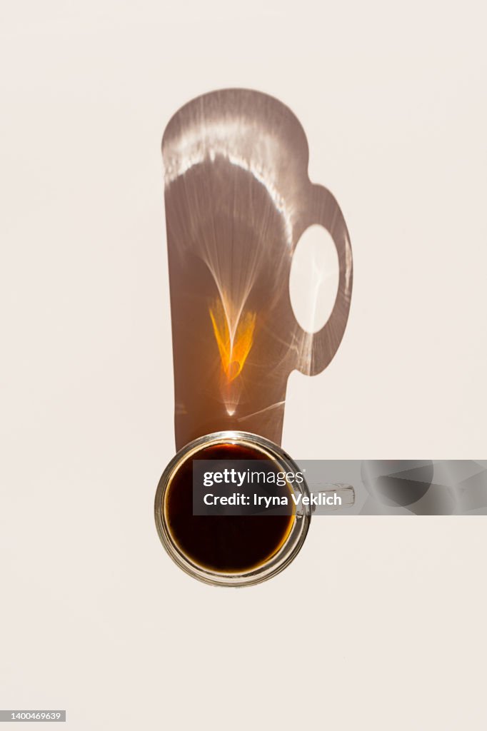 Aromatic morning coffee in glass cup and a long shadow from the cup on beige color background.