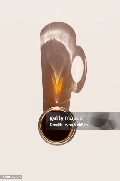 aromatic morning coffee in glass cup and a long shadow from the cup on beige  color background. - glass shadow stockfoto's en -beelden
