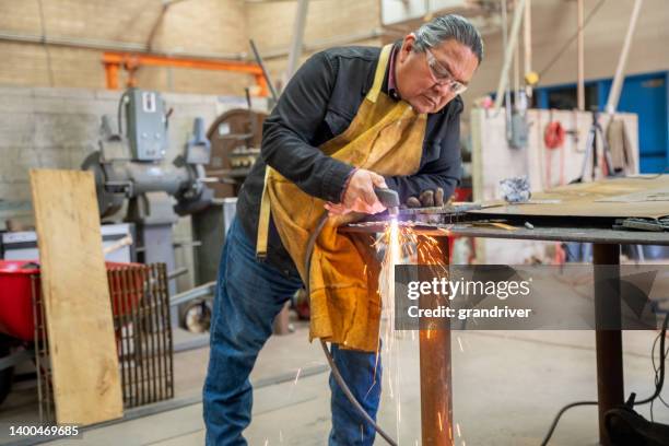 man in his fifties using a welder or cutting torch on a piece of steel in a metal workshop - minority groups stock pictures, royalty-free photos & images