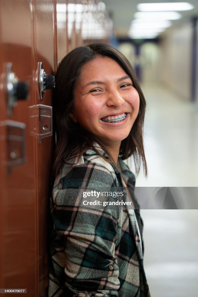Smiling Teenage High School Girl at her Locker in the School Hallway, Looking at Camera Portrait
