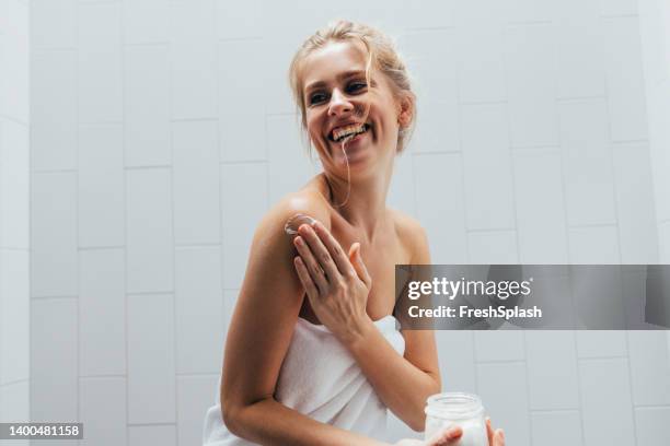 mujer rubia que se aplica loción después de una ducha - crema corporal fotografías e imágenes de stock