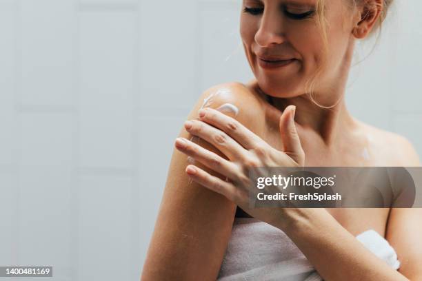 blonde caucasian woman applying body lotion - hydraterende creme stockfoto's en -beelden