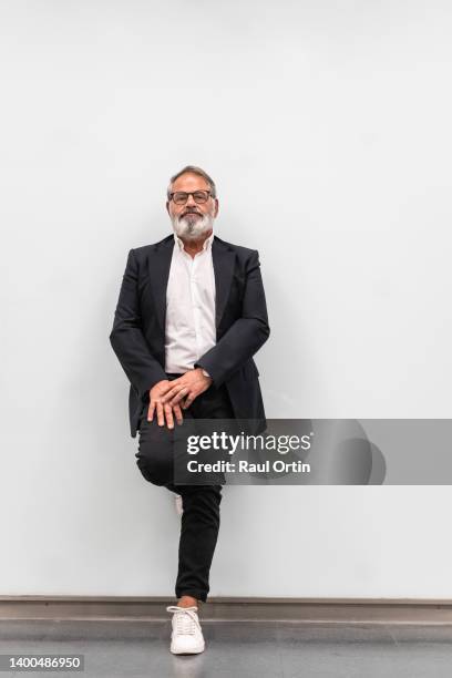 cheerful senior businessman standing in modern position against white wall - veste homme photos et images de collection